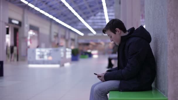 Tiener zittend op een bankje en het spelen van de smartphone — Stockvideo