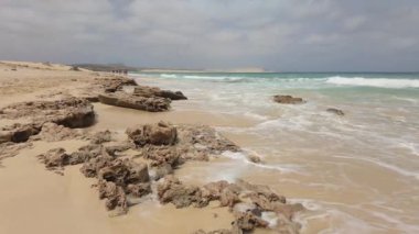 SAL REI, CAPE VERDE, AFRICA - MAYIS 01 2025: Kumlu bir plajda dalgalar ve Boa Vista Burnu 'ndaki volkanik kayalıklarda dalgalar gibi yürüyen tatilciler.
