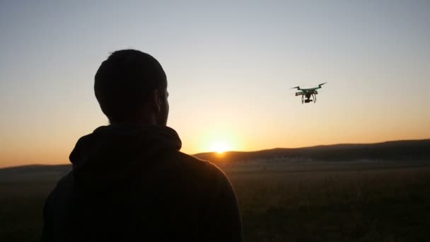 Un hombre controla un dron al atardecer — Vídeo de stock