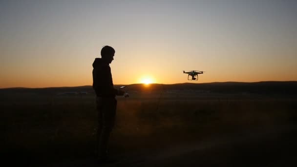 Um homem controla um drone ao pôr-do-sol — Vídeo de Stock
