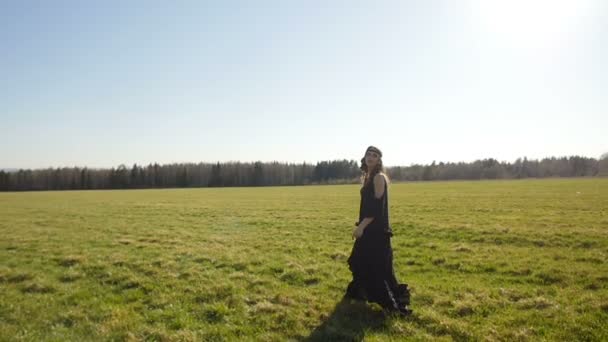 Mooi meisje in lange zwarte jurk wandelingen op veld — Stockvideo