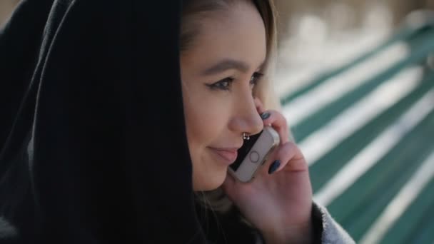 Jovem falando ao telefone enquanto sentado em um banco no parque — Vídeo de Stock