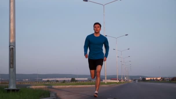 Ο τύπος που τρέχει κατά μήκος του δρόμου το ηλιοβασίλεμα. Μπροστινή άποψη — Αρχείο Βίντεο