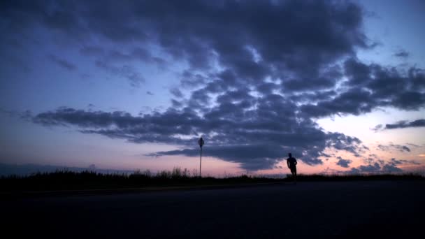 Silhueta de um homem correndo na estrada ao pôr do sol — Vídeo de Stock