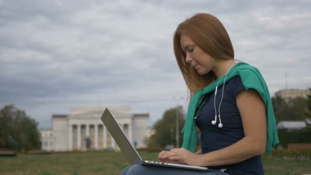 Студент сидит за ноутбуком рядом с университетом — стоковое видео