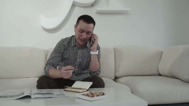 Hombre hablando en un móvil y escribe en un cuaderno — Vídeo de stock