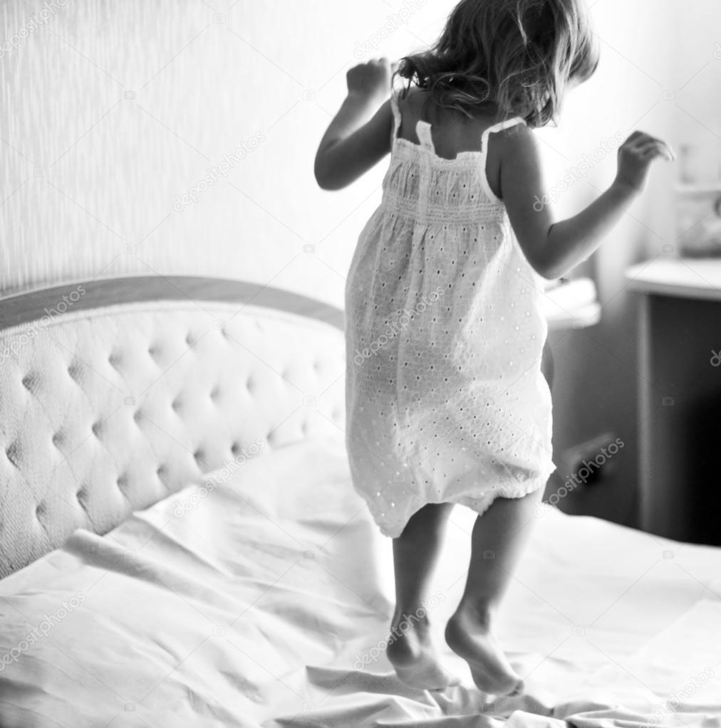 A dynamic indoor portrait of a little girl jumping on a bed