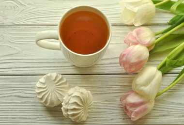 Rustik beyaz ahşap yüzeyüzerinde limon, taze lale ve iştah açıcı tatlılar ile bir fincan çay