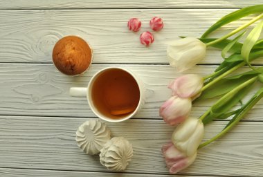 Rustik beyaz ahşap yüzeyüzerinde limon, taze lale ve iştah açıcı kek ile bir fincan çay