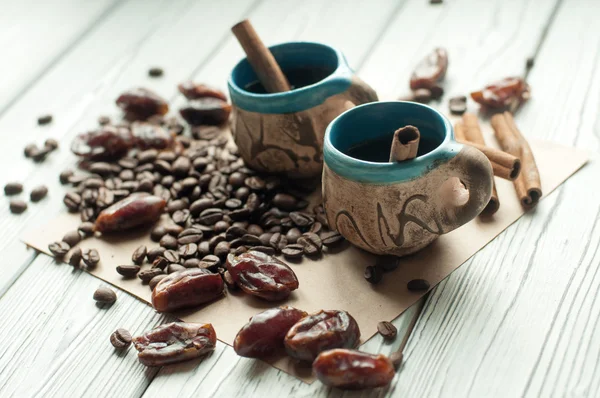Dua cangkir kecil buatan tangan tembikar kopi, biji kopi, kurma kering manis dan tongkat kayu manis — Stok Foto