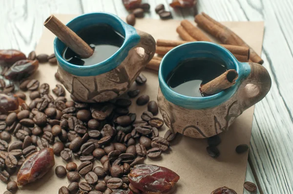 Dua cangkir kecil buatan tangan tembikar kopi, biji kopi, kurma kering manis dan tongkat kayu manis — Stok Foto