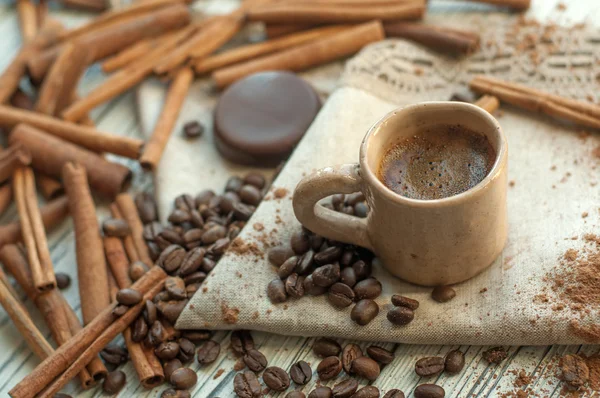 Una composición con una taza de barro hecha a mano de café, palitos de canela, granos de café, cacao en polvo y un caramelo de chocolate —  Fotos de Stock