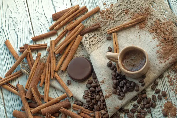 Una composición con una taza de barro hecha a mano de café, palitos de canela, granos de café, cacao en polvo y un caramelo de chocolate — Foto de Stock