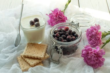 Taze çilek, ev yapımı yoğurt, bisküvi ve hassas beyaz kumaş yüzeyi parlak mor çiçekler bir cam kavanoz 