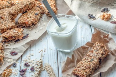 Bir bardak yoğurt ve bir beyaz tahta yüzey üzerinde el yapımı granola barlar  