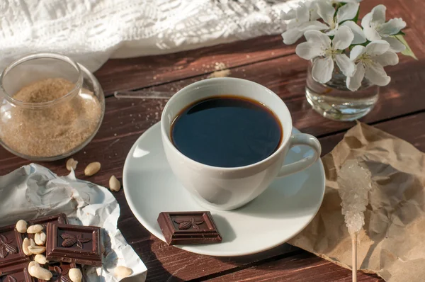 A composition with a cup of coffee, a chocolate bar and a blooming twig of an apple tree — Stock Photo, Image