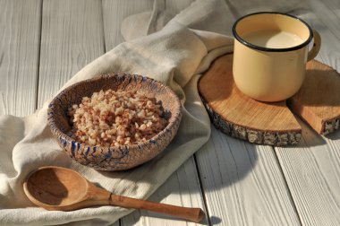 Buğday tahıl bir seramik kase haşlanmış, süt ve bir tahta kaşık bir rustik ahşap yüzey üzerinde metal bir kupa keten peçete ile dekore edilmiş 