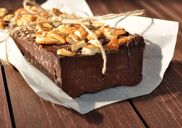 Un apetitoso pastel de chocolate decorado con pequeños trozos de galletas y colocado envuelto en un papel rústico —  Fotos de Stock