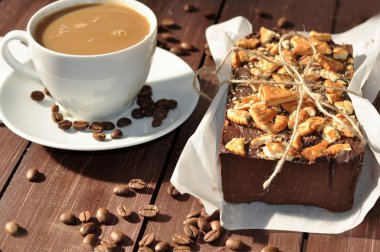 Bir fotoğrafı bir iştah açıcı bir çikolatalı kek bisküvi küçük parçalar ile dekore edilmiş ve rustik bir kağıt ve bir bardak süt kahve kaydırılan yerleştirilir