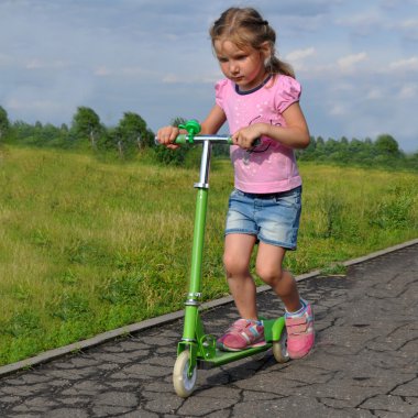 Küçük bir kız bir açık yaz manzara karşı bir scooter sürme