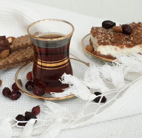 Una taza de té negro fuerte, una rebanada de pastel, palitos de canela, obleas y trufas de chocolate en un mantel blanco —  Fotos de Stock