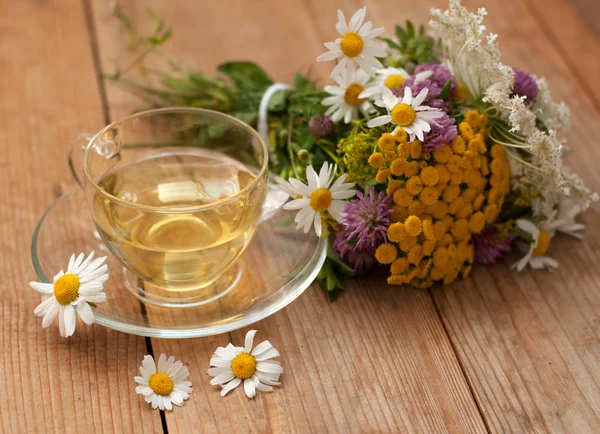 Une tasse de thé à la camomille dans une tasse en verre et un bouquet de fleurs d'été sur une surface en bois — Photo