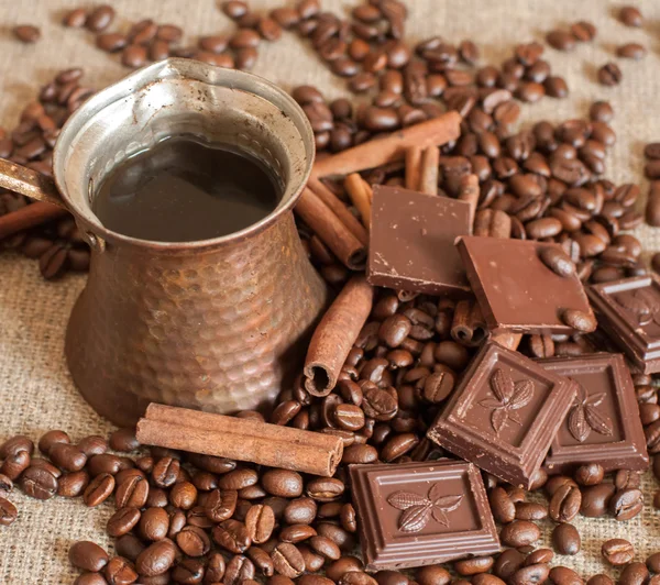 Sebuah teko kopi, biji kopi panggang, kayu manis tongkat dan potongan cokelat pada kain karung — Stok Foto