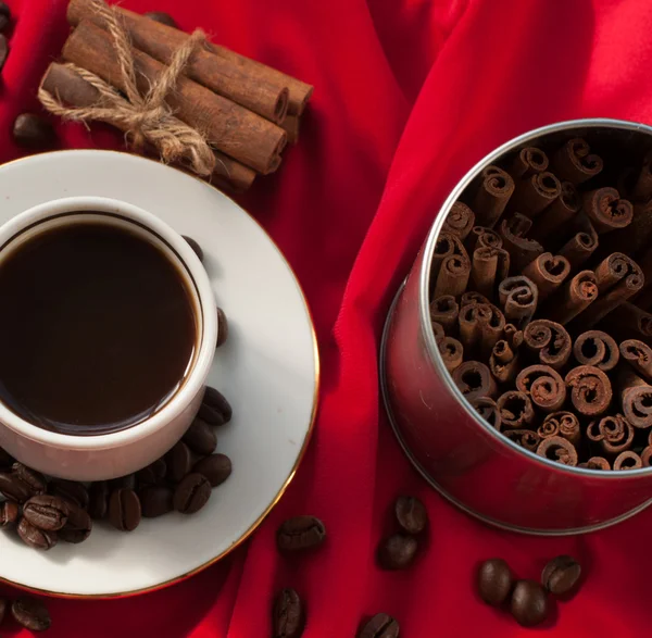 Secangkir kopi panas yang kuat, tongkat kayu manis dan biji kopi pada kain terbungkus merah — Stok Foto