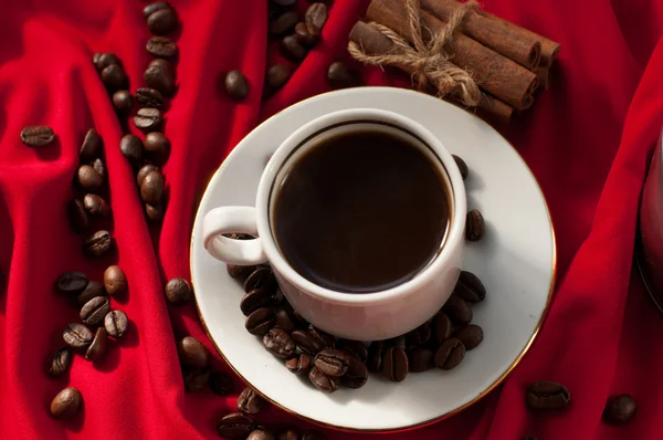 Secangkir kopi panas yang kuat, tongkat kayu manis dan biji kopi pada kain terbungkus merah — Stok Foto