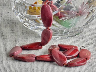 Doğal taş, düzensiz şekilli kırmızı Jasper boncukları kristal sepette taşlarla. Çuval bezi arka planı.