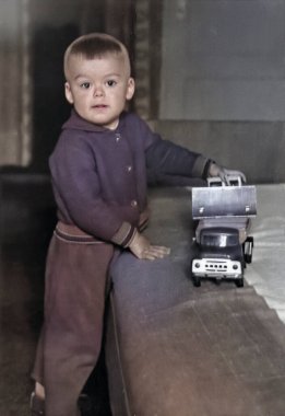 Oturma odasında oyuncak arabalarla oynayan küçük bir çocuğun klasik portresi. Şirin bir çocuğun komik fotoğrafı. 1970 'lerden kalma eski bir fotoğraf..