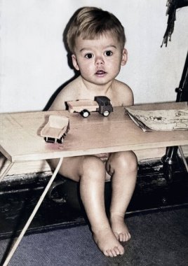 Oyuncak arabalarla bir masada oturan küçük bir çocuğun klasik portresi. Şirin bir çocuğun komik fotoğrafı. 1969 'dan kalma eski bir fotoğraf.