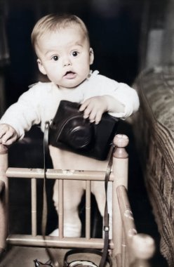 Beşiğinde duran küçük bir çocuğun klasik portresi. Çocuk elinde bir kamera kılıfı tutuyor. 1968 'den eski bir fotoğraf.