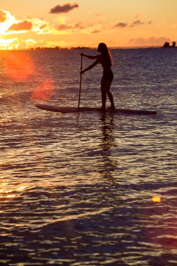 Kadın stand paddleboarding kadar güneş doğarken