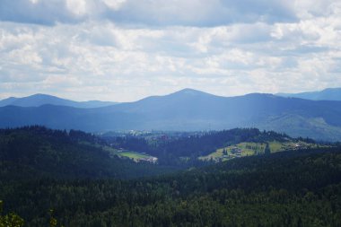 Ukrayna Karpat Dağları 'nın geniş panoramik manzarası, yuvarlanan yeşil tepeler, yoğun ormanlar ve beyaz bulutlu açık mavi bir gökyüzü. Doğa, manzara ve seyahat temaları için idealdir..