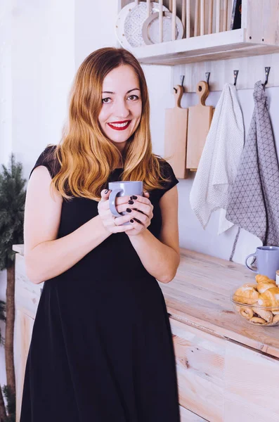 Portrait of smiling young woman with cup against kitchen interior background.