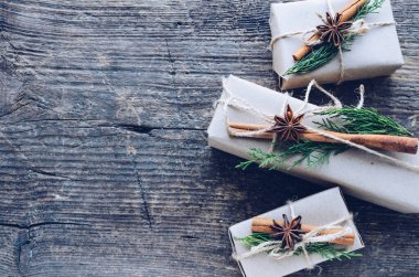 Modern Noel hediyeleri ahşap arka planda doğal dekorla paketlenmiş. İçinde sicim, yeşil dallar, tarçın çubukları ve anason bulunan el işi kağıt kutular. Mevsimlik tebrik kartı. Üst Manzara. Boşluğu kopyala.