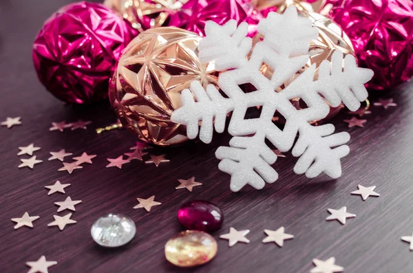 White snowflake on background of magenta and gold xmas baubles.