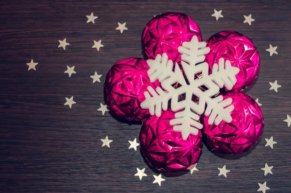 White snowflake and magenta xmas baubles on brown wooden background with stars. — Stock Photo, Image