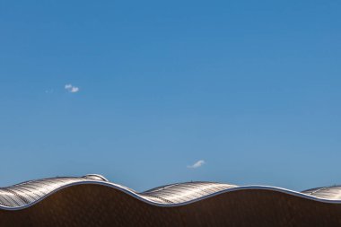 Mavi gökyüzü arkaplanına karşı dalgalı fütürist bina çatısı.