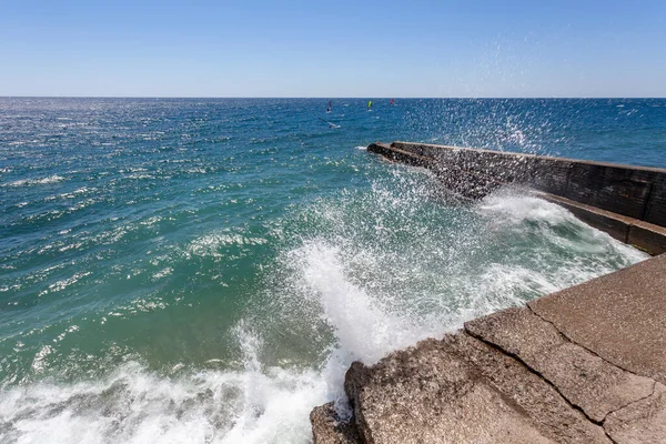 Dalgaların dalgaları dalgalanma suyuna çarpar. Arka planda rüzgar sörfçüleri dalgalarda sörf yapar..