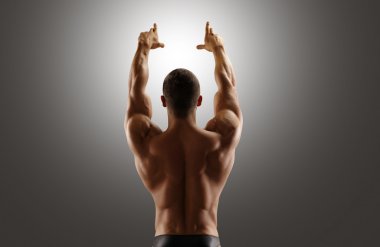 Kaslı adam ellerini yukarı kaldırarak sırt ile ayakta. Gri arka planı.