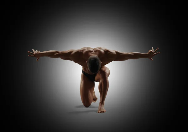 Junger muskulöser Mann auf einem Knie stehend, die Arme zur Seite. schwarzer Hintergrund. — Stockfoto