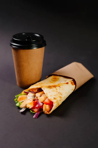 Tavuklu shawarma ve siyah arka planda kağıt bardakta içki. Bir sokak kafesinde öğle yemeği. Fast food kafe. Tavuklu Shawarma ve kağıttan yapılmış bir fincan kahve..