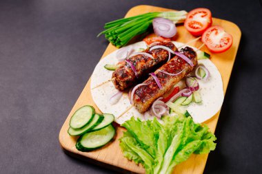 Pita ekmeğinde ızgara lula kebabı ve arka planda sebzeler.