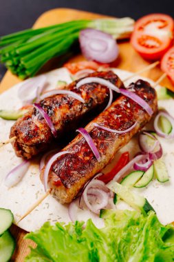 Pita ekmeğinde ızgara lula kebabı ve arka planda sebzeler.