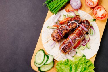 Pita ekmeğinde ızgara lula kebabı ve arka planda sebzeler.