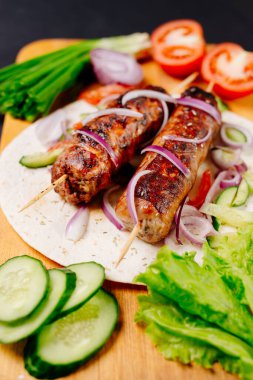 Pita ekmeğinde ızgara lula kebabı ve arka planda sebzeler.