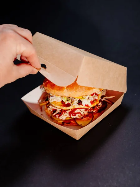 Bir adamın eli arka planda hamburger kutusunu açar. Köfteli hamburger ve arka planda karton bir kutuda omlet..