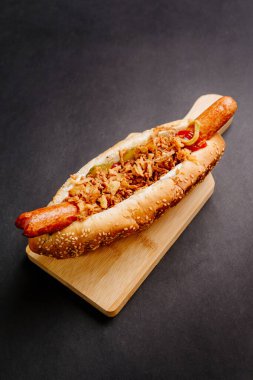 Kızarmış sosisli sandviç, ketçap, hardal sosu ve siyah zemin üzerinde çiğ ve kızarmış soğan.